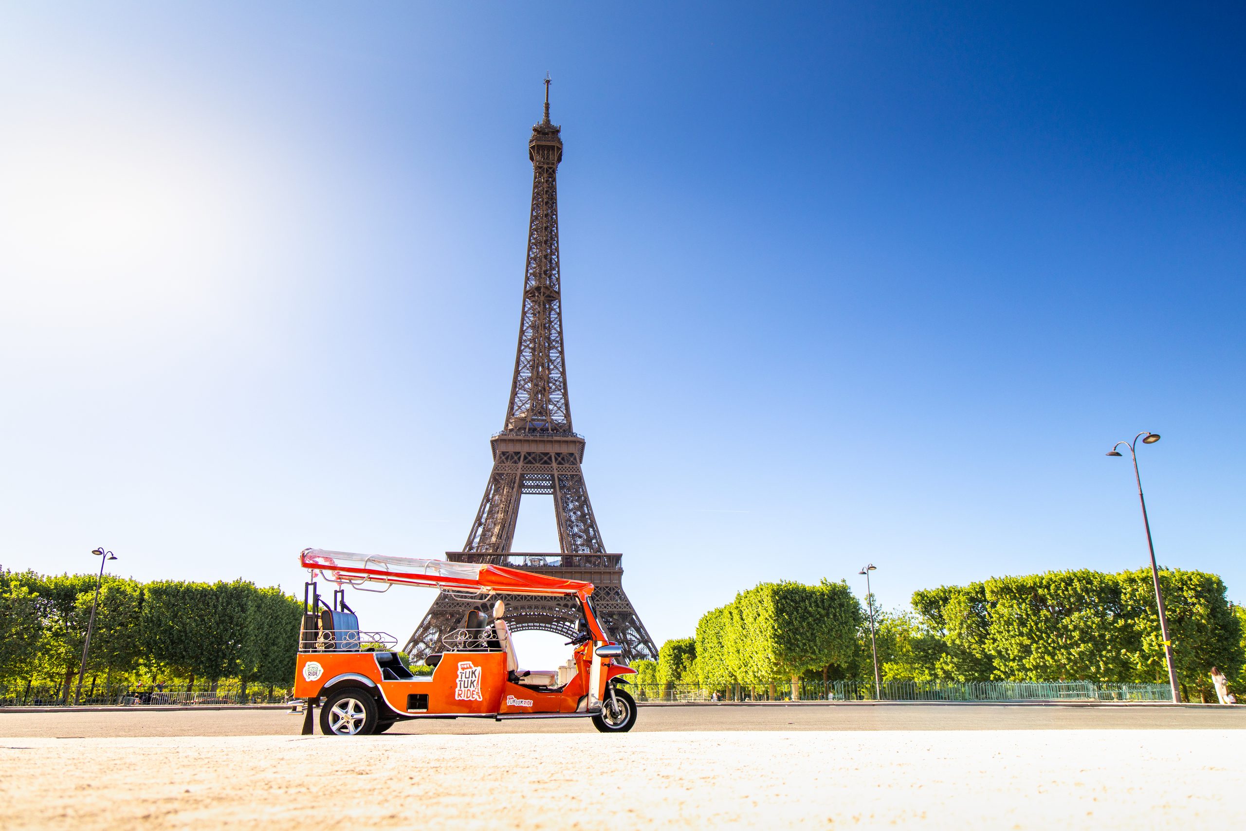 Tuktuk électrique orange aux pieds de la Tour Eiffel