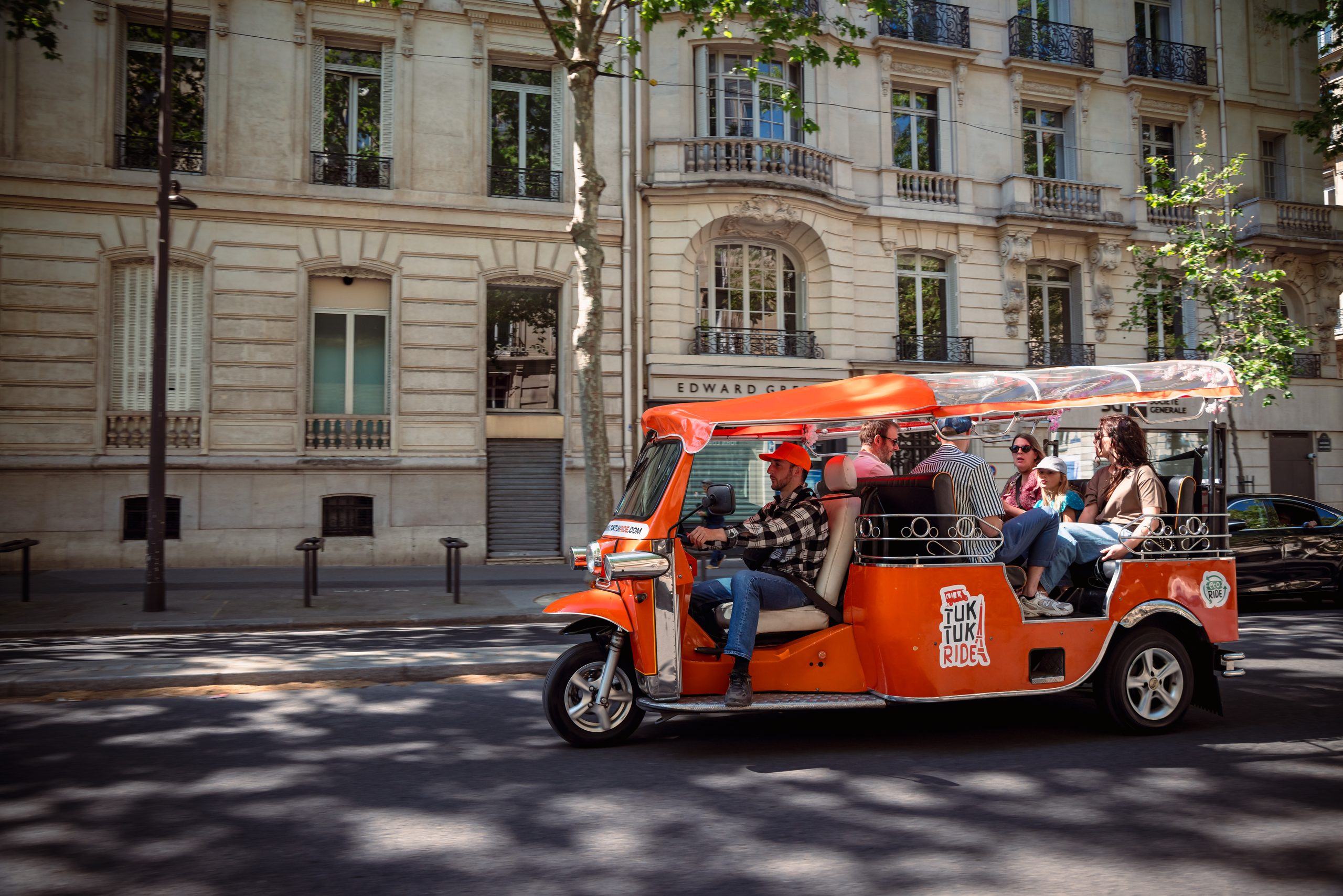 Tuktuk orange dans une rue haussmannienne de Paris
