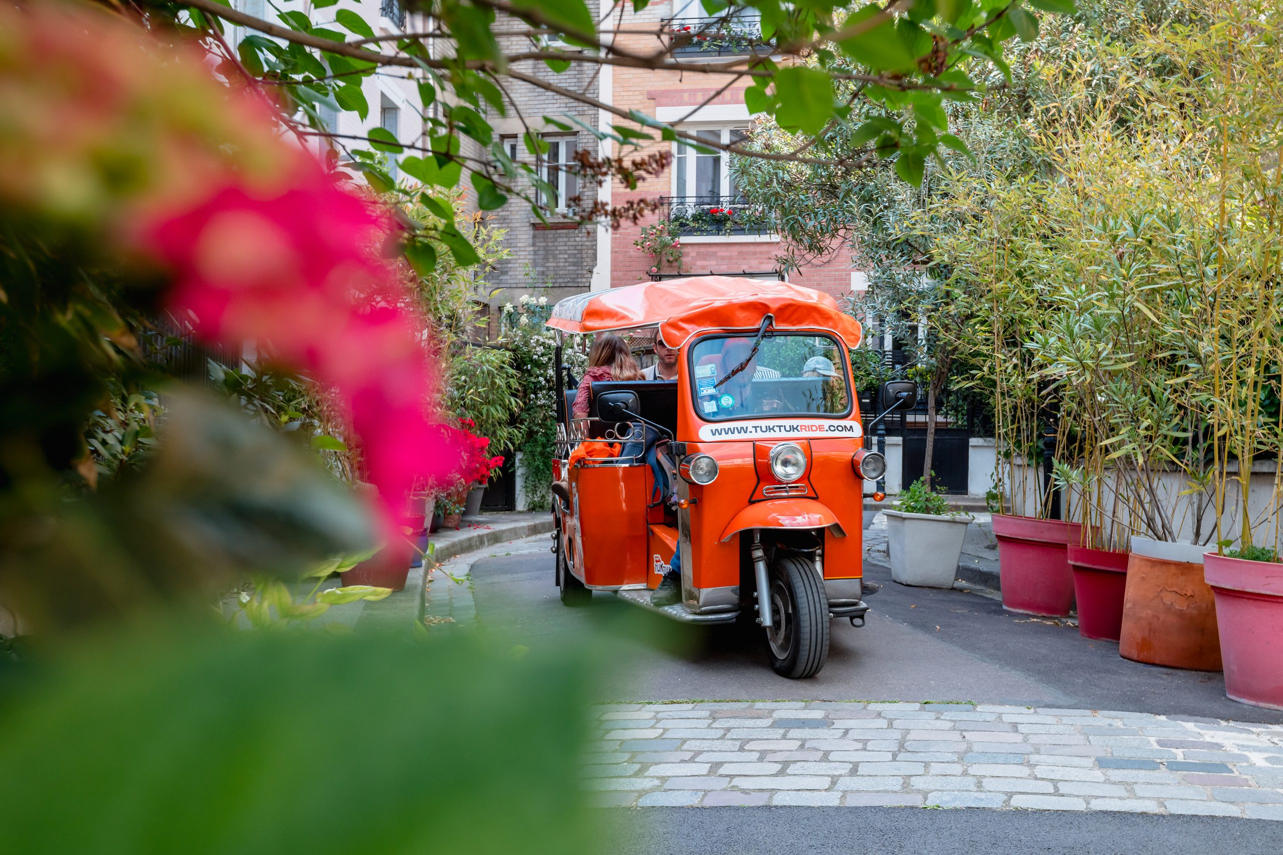Tuktuk électrique orange dans une ruelle parisienne fleurie