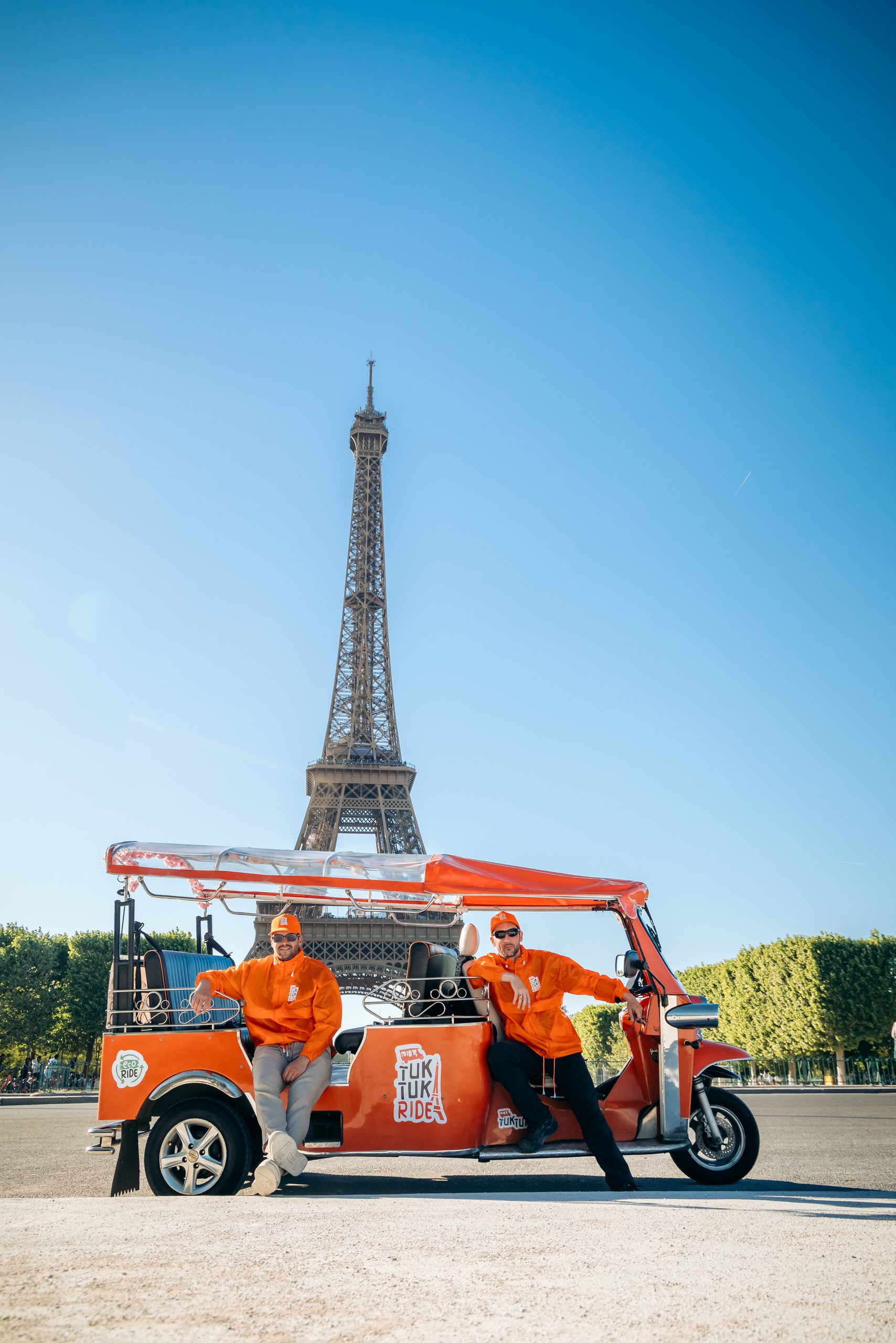 Tuktuk électrique orange devant la Tour Eiffel à Paris
