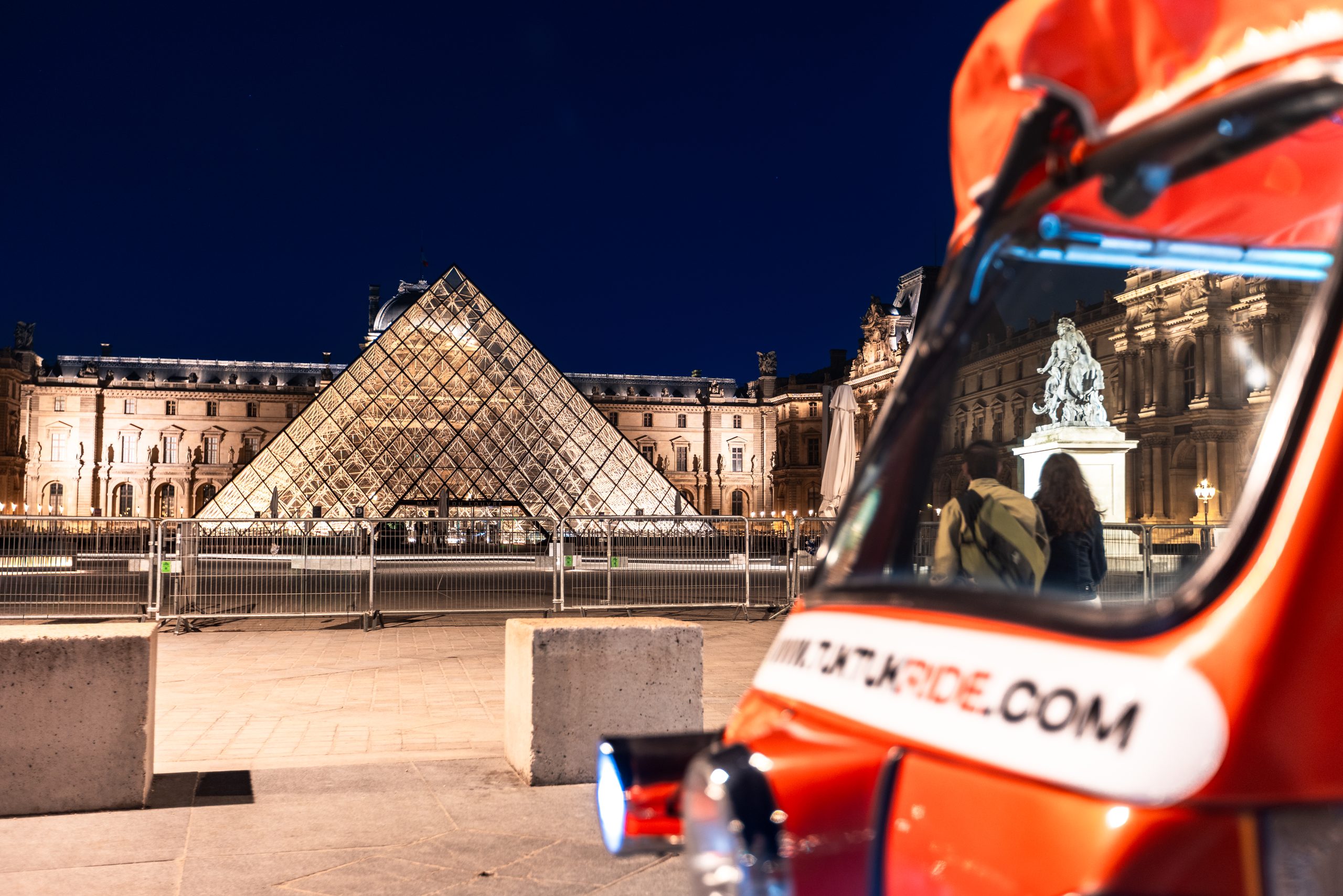 Tuktuk orange devant la pyramide du Louvre illuminée la nuit