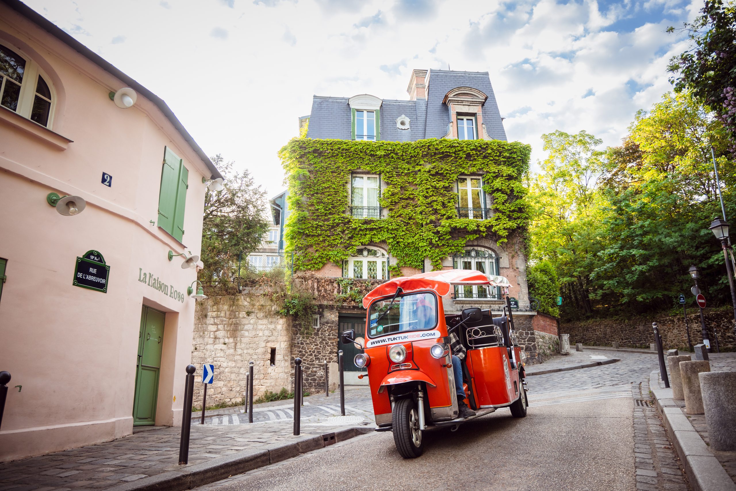 Tuktuk rouge devant un immeuble couvert de lierre à Paris