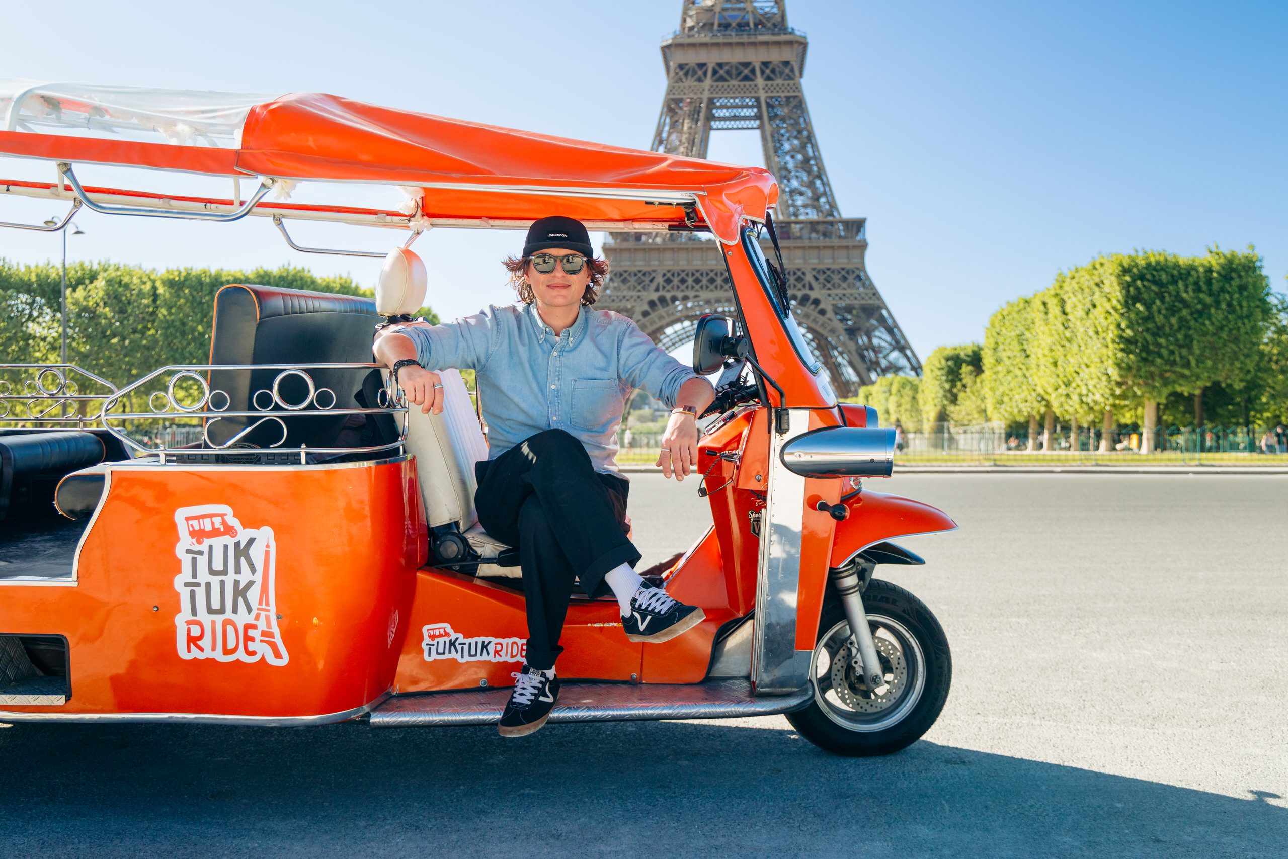 Tuktuk orange avec chauffeur devant la Tour Eiffel à Paris